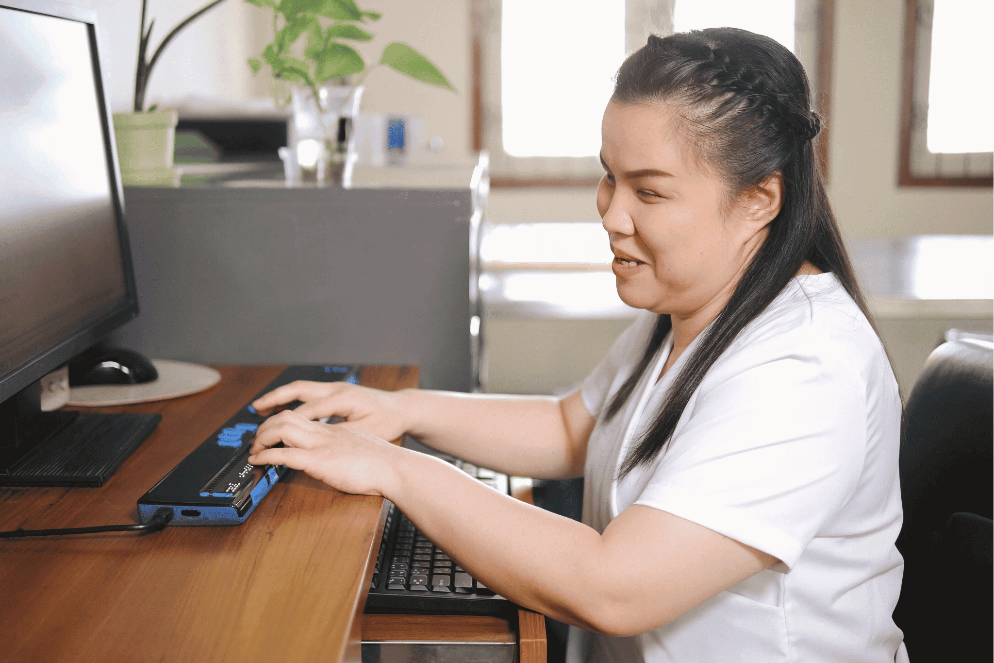 Eine Frau mit Sehbehinderung sitzt am Computer. Sie schreibt auf einer Braille Tastatur.