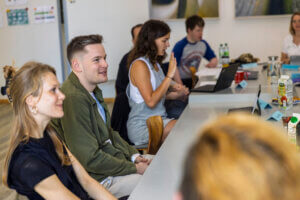 Mehrere Menschen sitzen in einem Workshop an einem langen Tisch und sprechen.