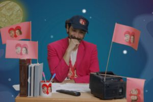 Eine Person sitzt am Schreibtisch und schaut auf einen kleinen Mini-Fernseher.